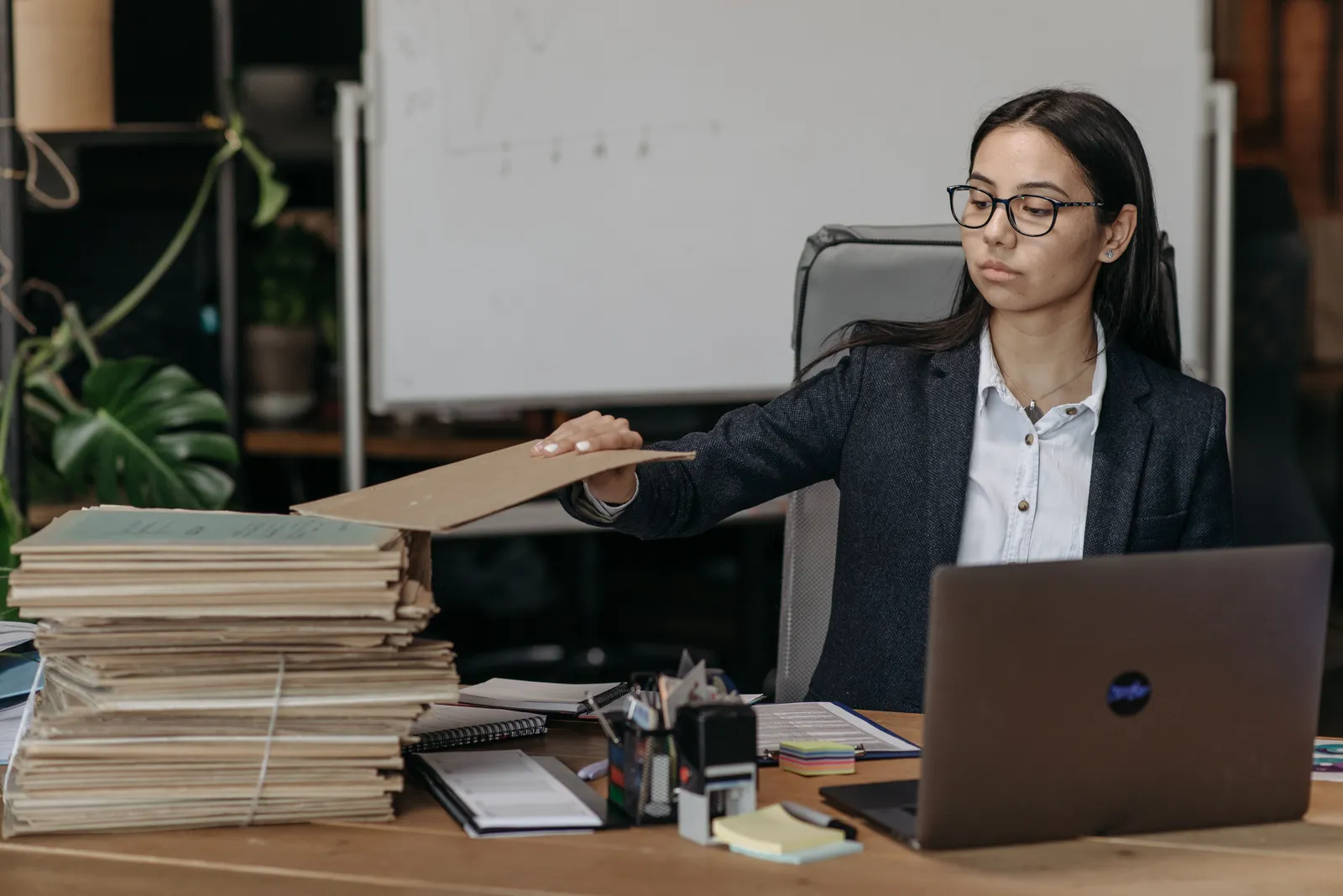 femme assise à un bureau chargé de dossiers, qui tend le bras pour attraper l'un d'eux