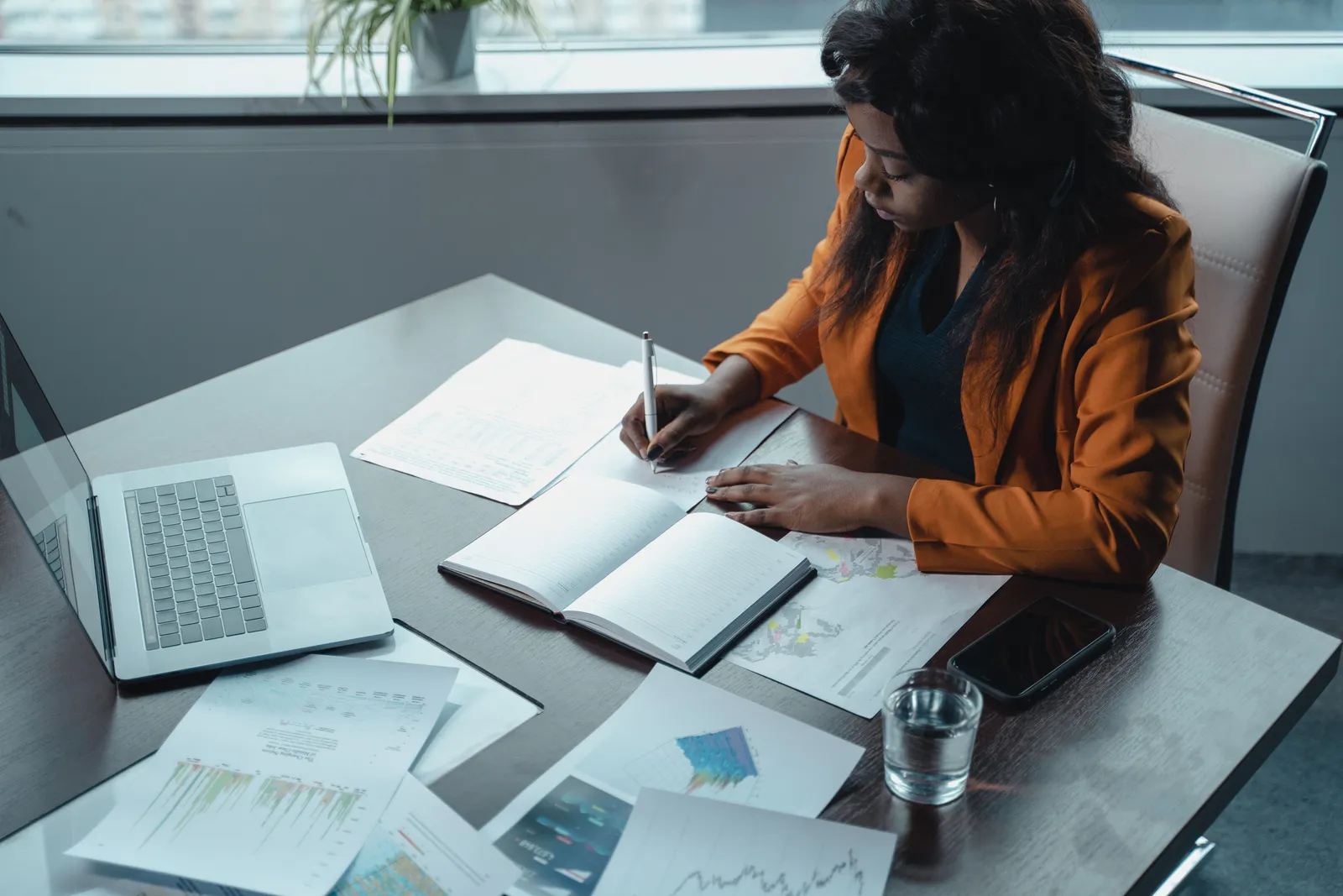 femme travaillant, bureau chargé avec laptop, carnet et documents avec des graphiques divers